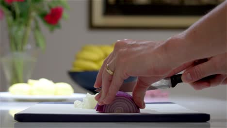 Side-view-close-up-of-someone-slicing-a-red-onion-on-a-chopping-board