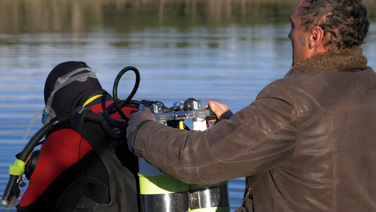A man helps a diver open his oxygen cylinders