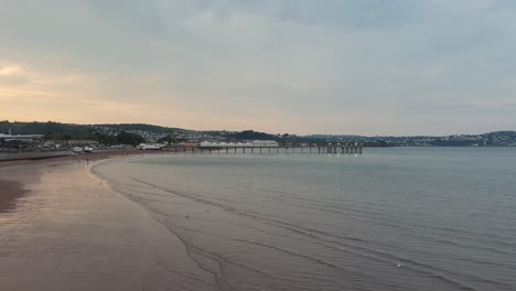 Scenic-landscape-view-of-Paignton-beach,-pier,-and-ocean-during-dusky-sunset-in-Devon,-England-UK