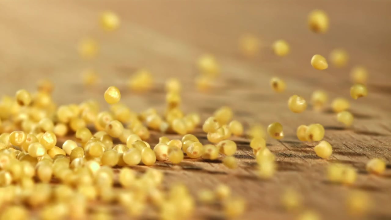 Chicchi di miglio crudo che cadono e rimbalzano su una superficie di legno.