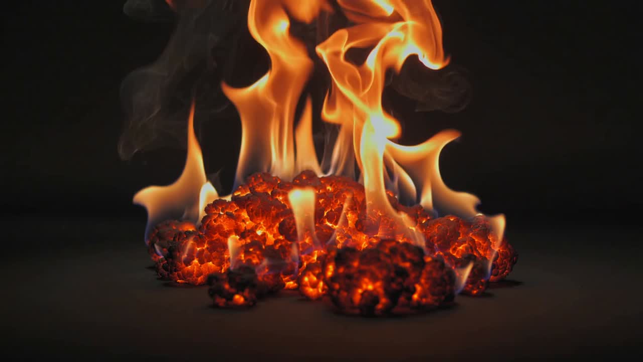 Heat from embers producing taller orange flames on flat dark surface, releasing smoke