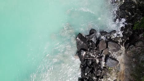 Peaceful-aerial-wide-shot-of-water-crashing-on-the-rocks-on-beach-shore-sand-blue-sky-white-clouds-turquoise-water-relaxation-vacation-tourism