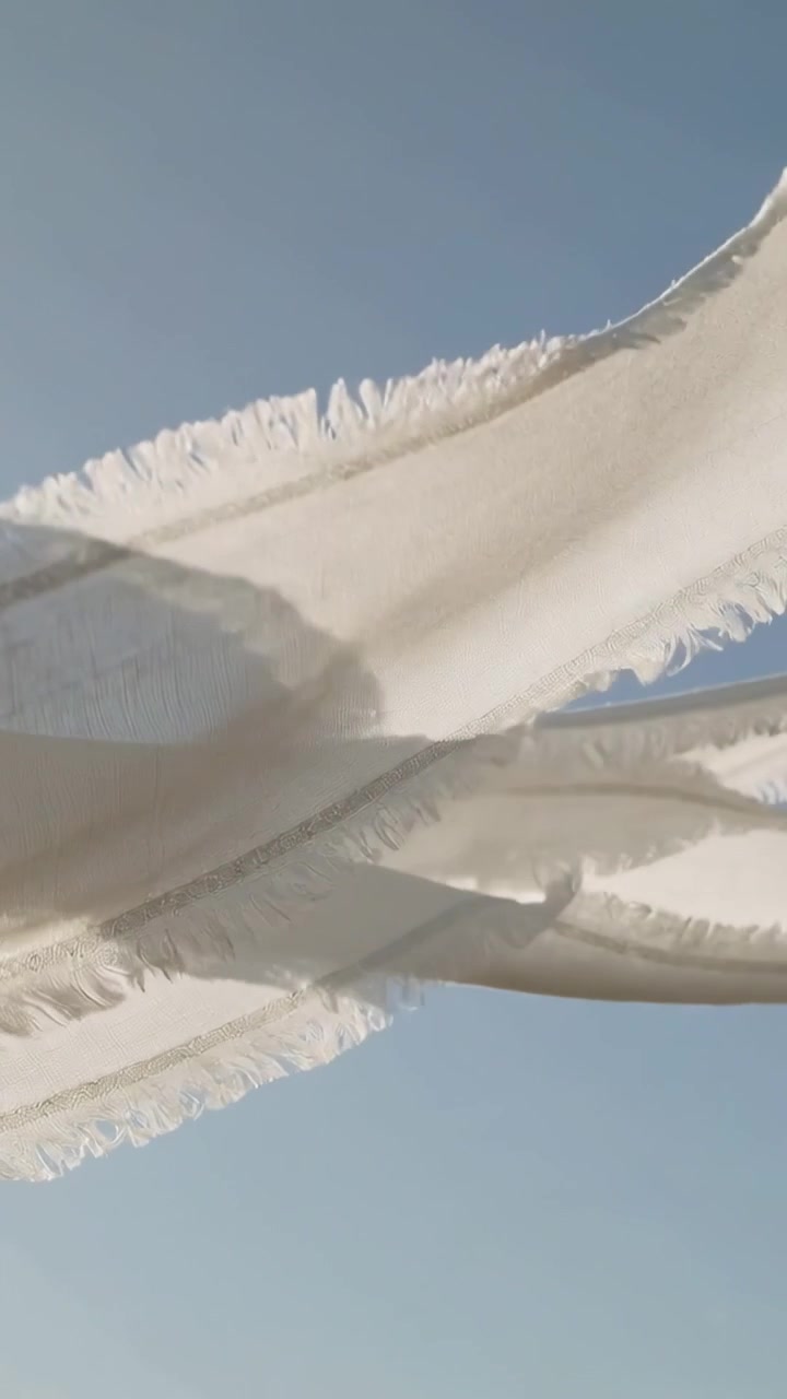 Video verticale: Pannelli bianchi frangiati che ondeggiano appesi sotto un cielo blu, raffiche di vento che sollevano i bordi