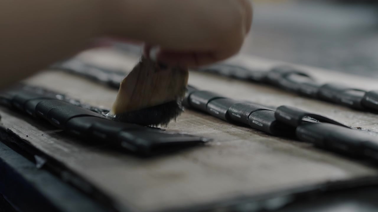 Worker applies adhesive to leather shoe parts on a workbench in a factory setting