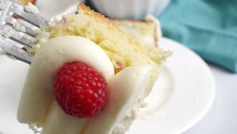 making a dessert called red raspberry tea cake made with fresh berries and vanilla buttercream frosting. great for tea parties. cutting a piece of the raspberry tea cake with a fork on a white plate