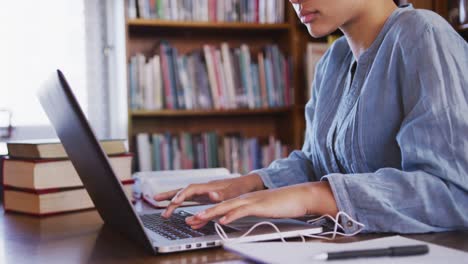 Asiatische-Studentin,-Die-Einen-Blauen-Hijab-Trägt,-Sitzt-Und-Benutzt-Einen-Laptop-In-Der-Bibliothek