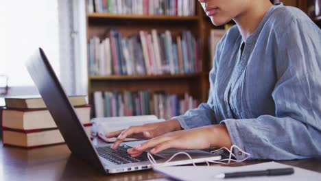 estudiante asiática con un hijab azul sentada y usando una computadora portátil en la biblioteca