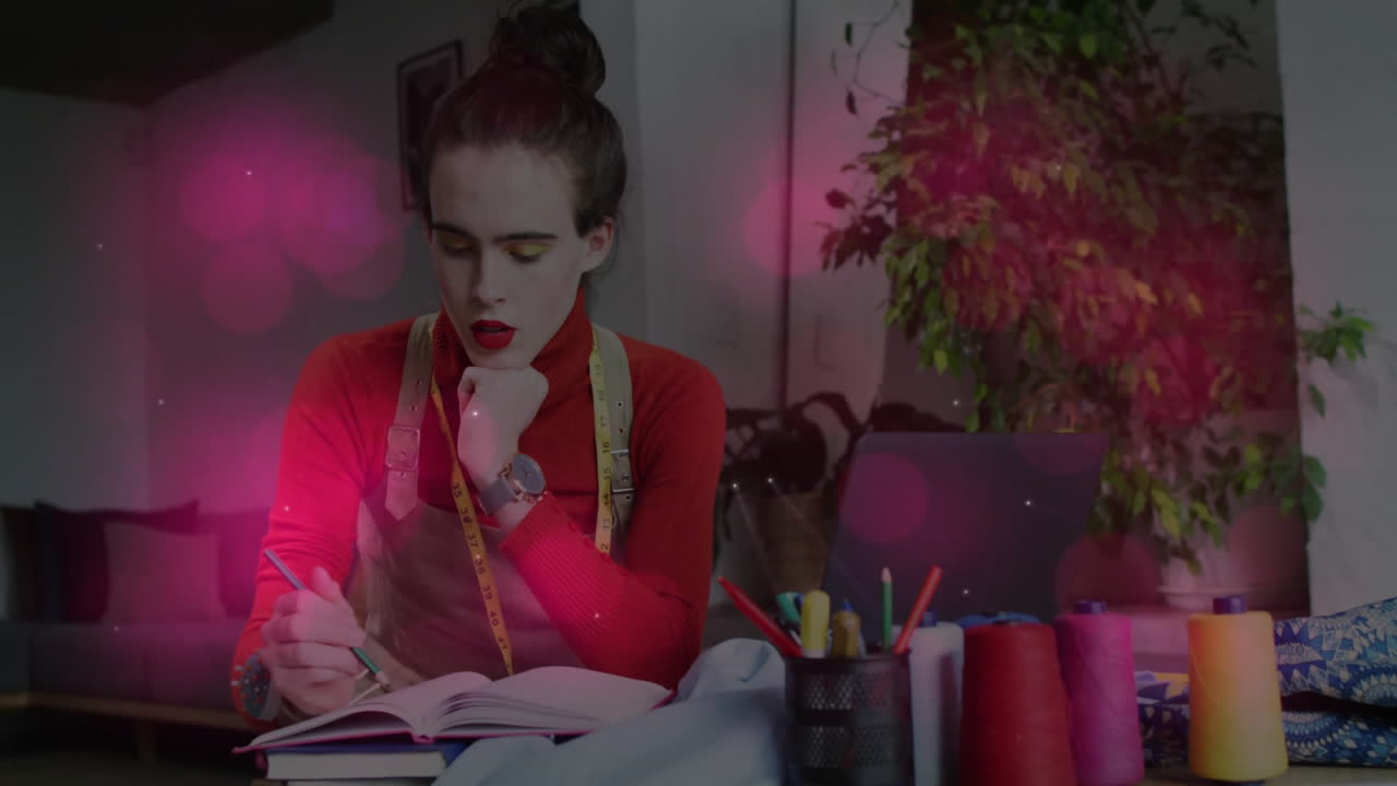 Woman sketching business plan in studio, showcasing animated pink flares around laptop and notebook