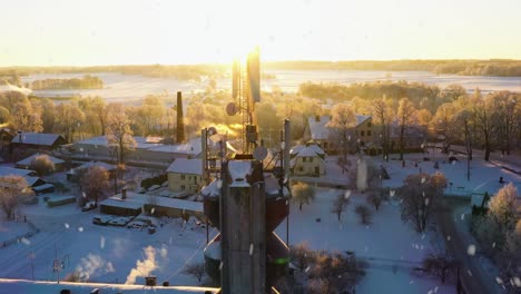 cell antenna tower in small rural town on snowy sunny winter day, aerial orbit view