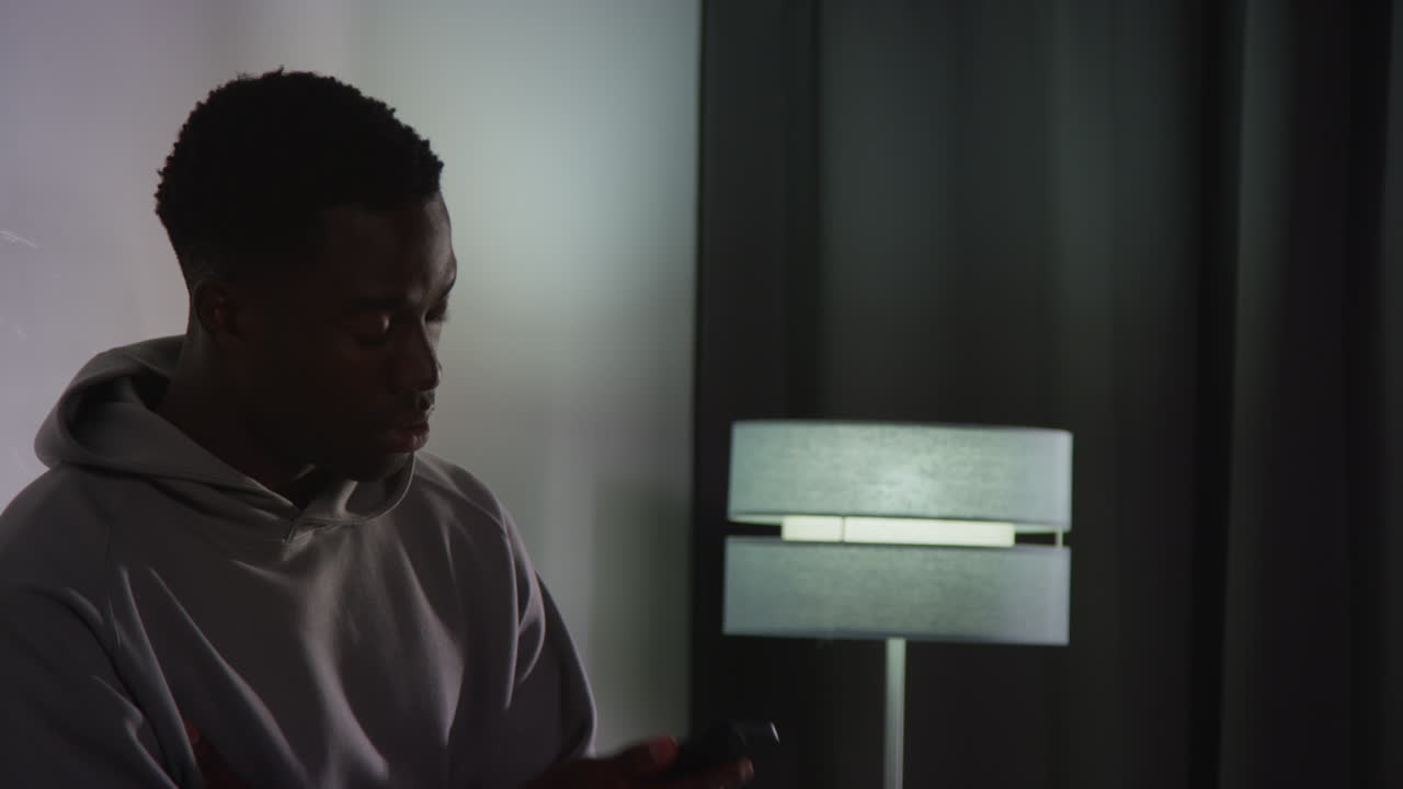 joven infeliz y deprimido de pie contra la pared en casa hablando por teléfono móvil en la noche