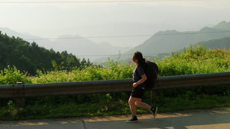 slow motion of young female asiatic solo traveller walk-in with backpack on mountains road enjoying the panoramic view over the valley