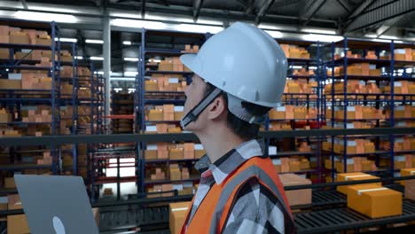 close up side view of asian male engineer with safety helmet looking at a laptop and looking around while standing in the warehouse with shelves full of delivery goods