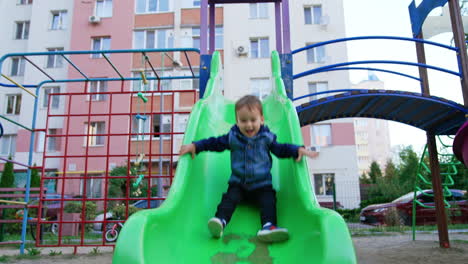 little kid sits on the big green slide. happy kid slides down approaching camera. low angle view.