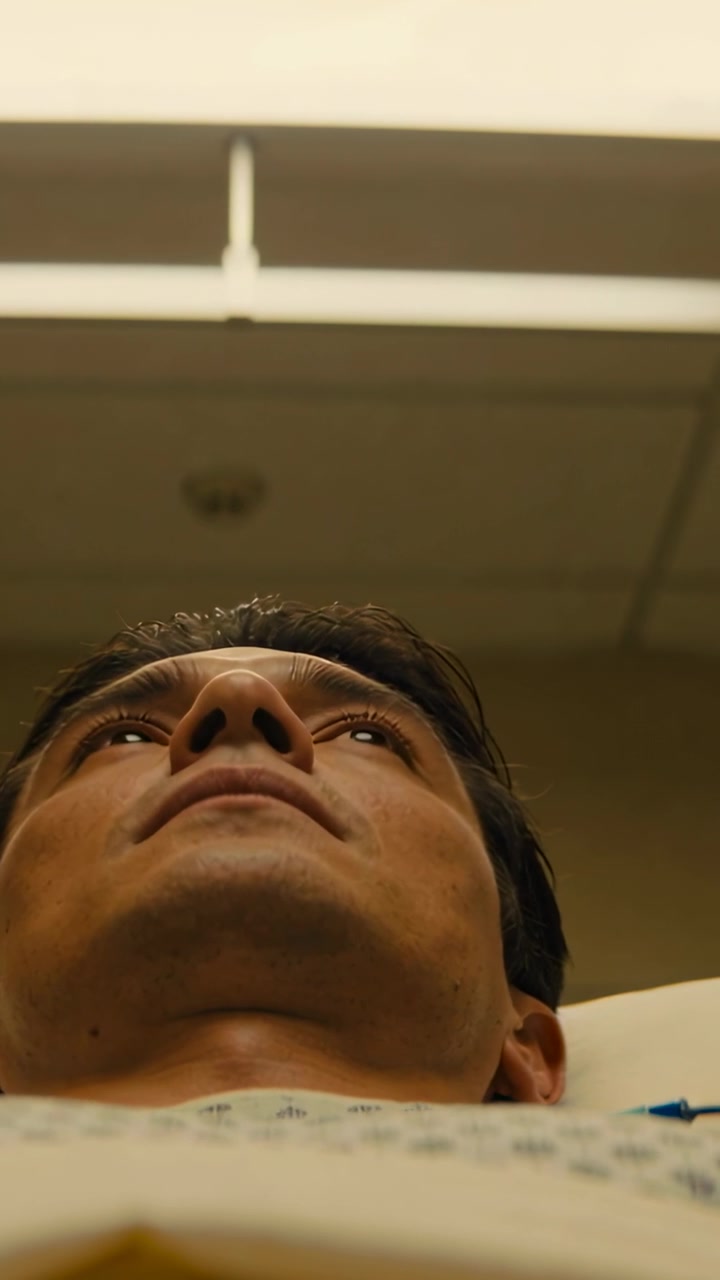 Vertical video: Blinking man in hospital gown shifting gaze toward ceiling fixture in hospital bed