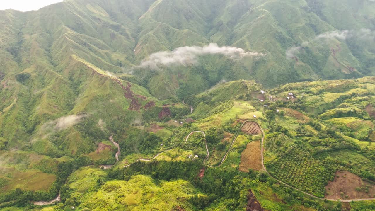 Cinematic aerial view of lush green mountains with winding roads, farms, and misty clouds, perfect for nature, travel, agriculture, and landscape projects
