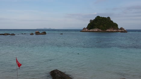 an aerial shot or footage of a clear ocean with small island on the side with green trees