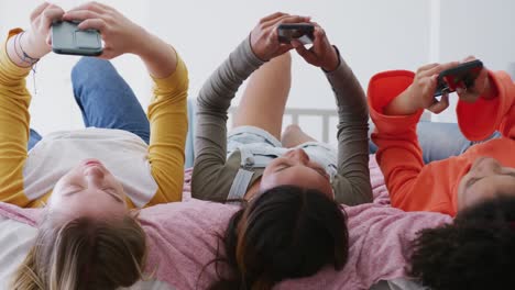 happy diverse teenager girls friends lying on bed and using smartphones, slow motion