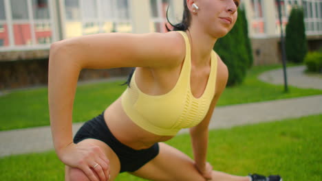 a young woman with headphones is stretching on the grass in a city park in slow motion. listen to music while playing sports