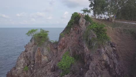 a slow and smooth cineamtic reveal shot flying above a rocky viewpoint revealing a curvy road below a mountain in the distance, thailand