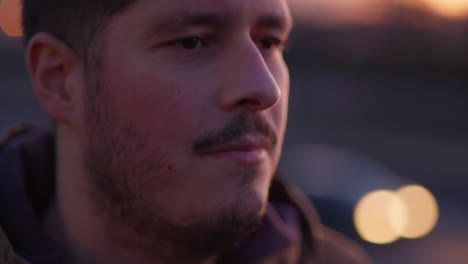 an extreme close-up of a man's face with no emotion, as a blurry highway with cars passing by appears in the background during dusk. slow-motion shot for a dramatic and cinematic effect.