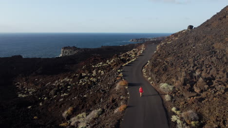 Romantic-view-of-a-road-in-the-mountains-overlooking-the-rocky-sea-and-a-woman-with-fluttering-hair-and-a-dress-in-the-wind---aerial-forward-shot,-Hierro-island,-Canary---aerial-forward-shot