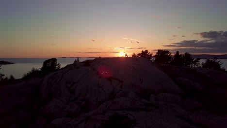 Inukshuk-En-La-Cima-De-La-Isla-Rocosa-De-Pinos-Al-Atardecer,-Antena-De-Drones-En-órbita-Amplia