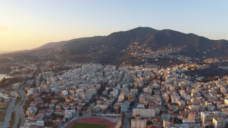 sunrise aerial drone flight over mountains to downtown mitilini revealing sea with ferry to athens, lesvos, greece