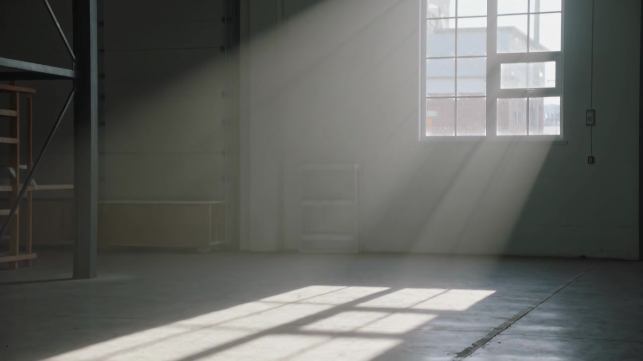 Luce solare che filtra attraverso una finestra a riquadri, con un raggio che scivola sul pavimento dello studio rivelando un'ombra a griglia.