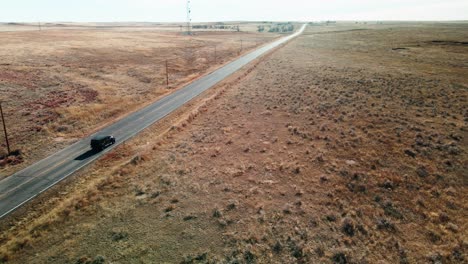 Black-all-terrain-car-driving-on-a-highway-in-a-dry-and-desert-landscape