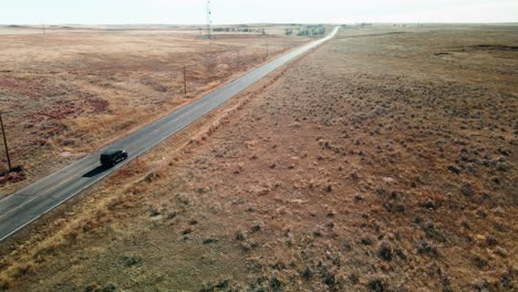 black all-terrain car driving on a highway in a dry and desert landscape