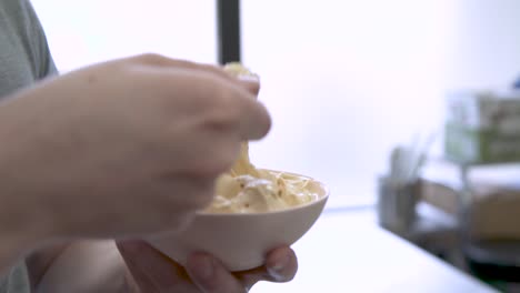 hand stirring and scooping cup of gelato with yellow spoon