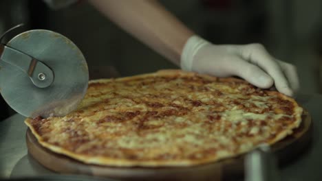 un primer plano de la mano del chef cortando pizza en la cocina.