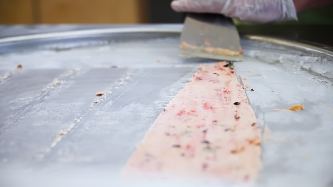 la espátula recoge lentamente el helado enrollado tailandés del plato frío, cámara lenta de cerca 4k