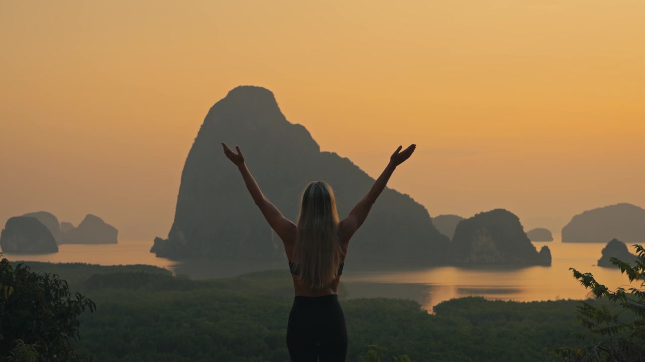 Fit sarışın bir kadın, altın saatte tropikal kireçtaşı kaya adalarını izlerken yukarı selam dua pozunu yapıyor. Büyüleyici doğal bir deniz manzarasında huzurlu bir yoga anı.