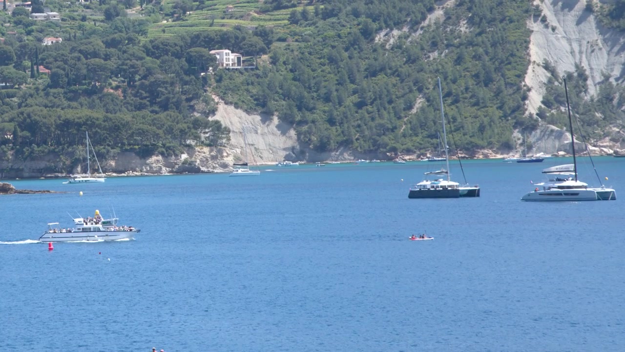 Inquadratura ampia di barche ancorate in acqua blu contro una lussureggiante scogliera costiera verde.