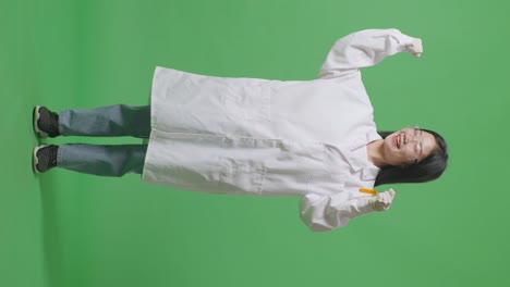 실험관에 오렌지색 액체가 들어있는 아시아 여성 과학자의 몸이 가득 차 있습니다. 실험실의 녹색 스크린 배경에 서있는 동안 미소 짓고 을 구부리고 있습니다.