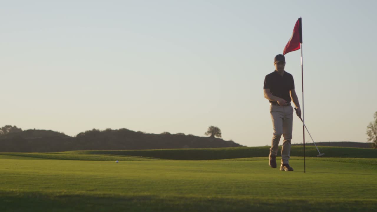 un golfista quita una bandera de un hoyo en un campo de golf
