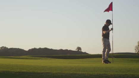 a golfer removes a flag from a hole on a golf course