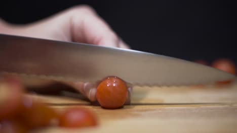 Close-up-shot-of-someone-cutting-cherry-grape-tomatoes-on-cutting-board-with-black-background