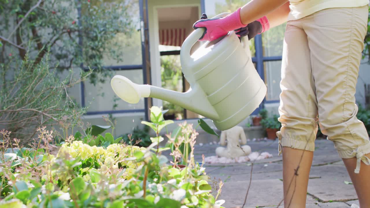 hija de raza mixta haciendo jardinería en un jardín soleado, regando plantas