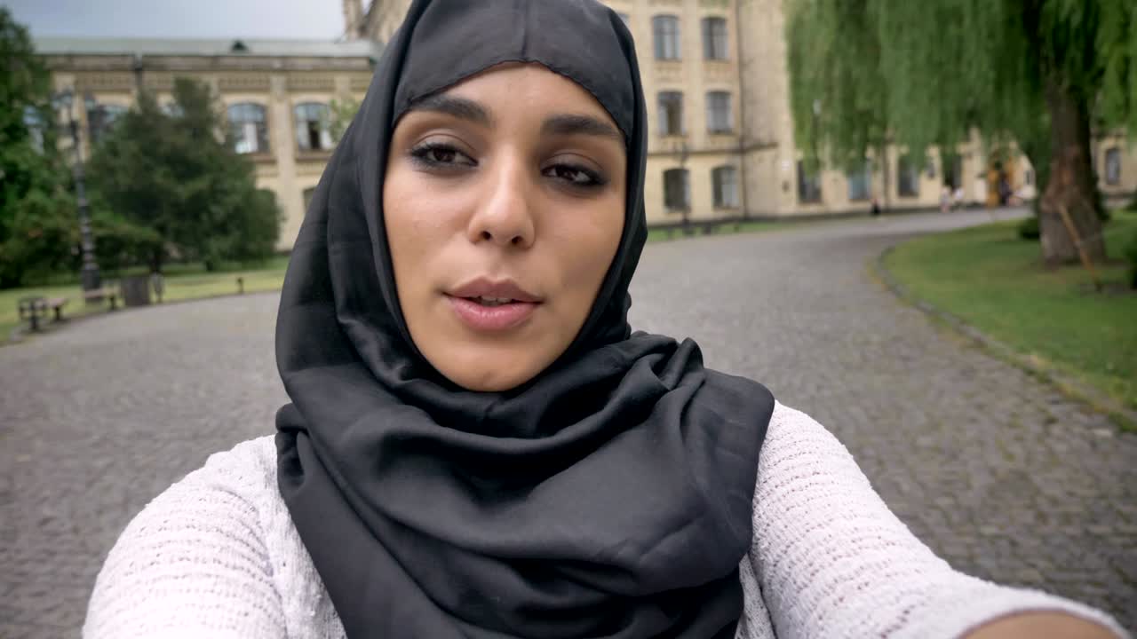 Young happy muslim woman in hijab is making video in blue weather, communication concept, religious concept, building on background
