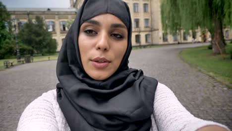 young happy muslim woman in hijab is making video in blue weather, communication concept, religious concept, building on background