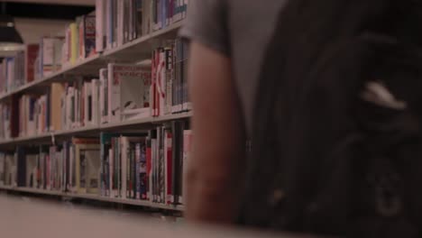 Person-Walks-Through-Library-While-Examining-Books-On-Display