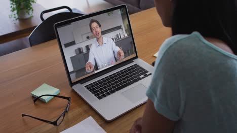 Mixed race businesswoman sitting at desk using laptop having video call with male colleague