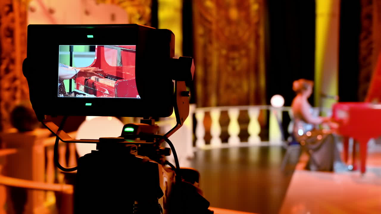 Professional camera filming a woman playing a red piano on the backstage of a TV set