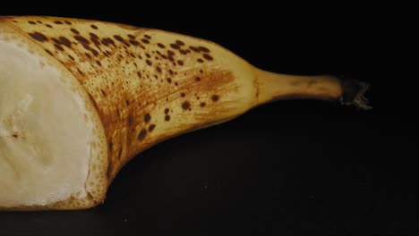 cinematic smooth pan across a cut ripe banana, captured against a black background and studio lighting