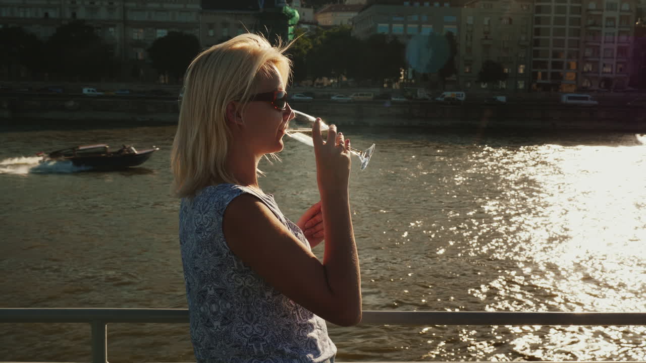 와인 한 잔을 들고 있는 여자가 강 유람선을 타고 여행하고 있다
