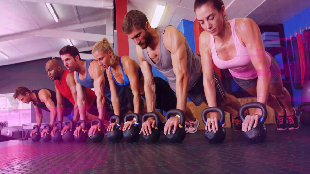 Grupo de seis pessoas na academia reagindo a um sinal fora da tela, abaixando e levantando kettlebells com pausas para força.