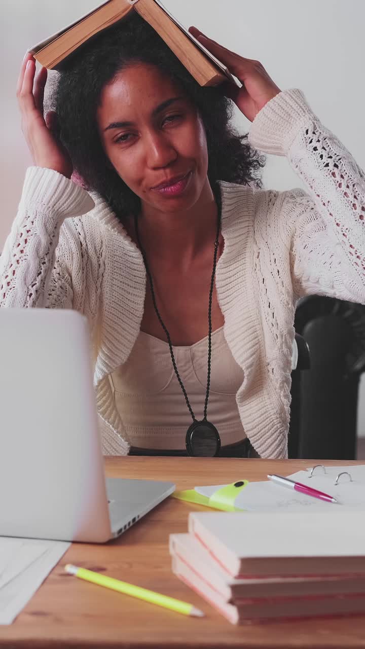 Young funny african american business woman fooling with book sits at workplace