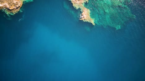 Drone-shot-over-crystal-clear-water-and-rocky-shore-in-Cirkewwa-Malta
